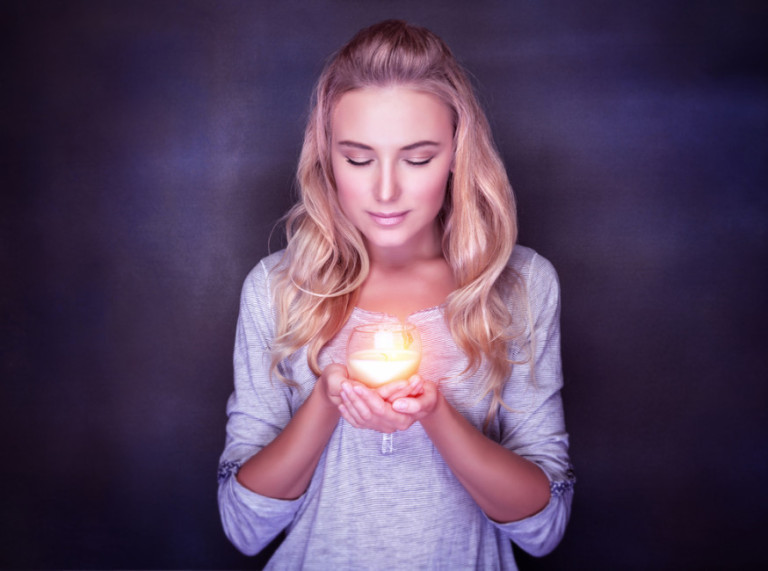 woman looking down at candle cradled in hands