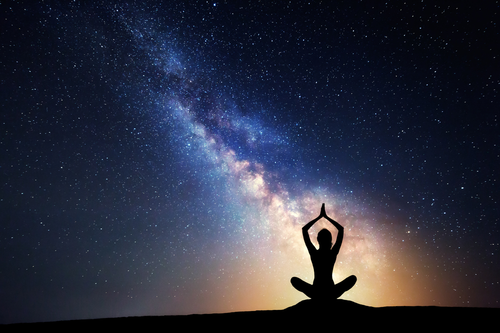 person meditating silhouetted in front of Milky Way galaxy with a soft golden aura around them