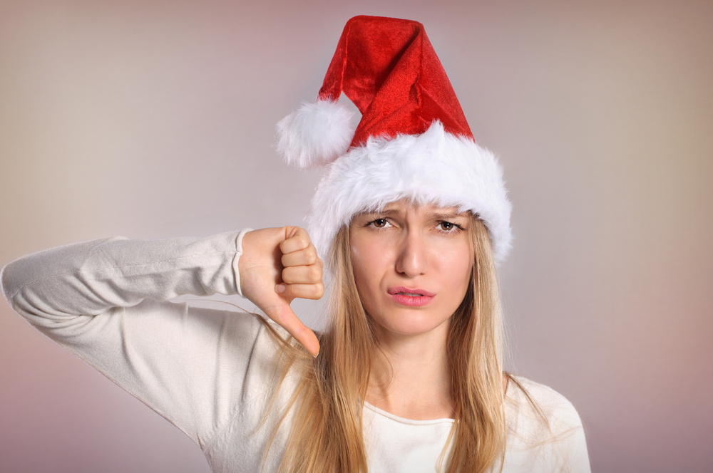 Annoyed-looking woman in Santa hat giving a thumbs-down. Holiday distress, Christmas boredom.
