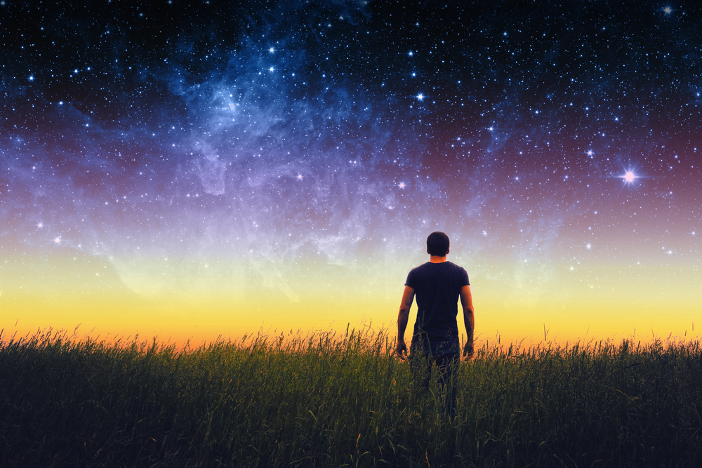 Empowered man standing in field looking up at beautiful universe sky.