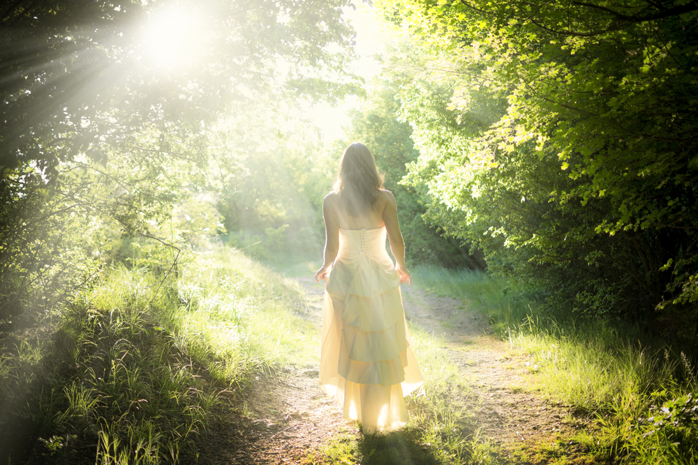 How can you be a lightworker on a practical level? Woman walking down sunlit path in nature.
