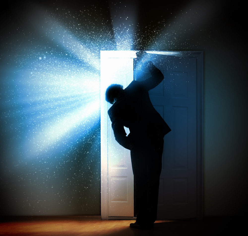 Man in dark room opening door to let in brilliant light