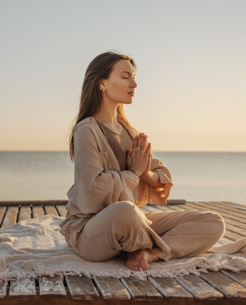 Calm young caucasian woman is meditating while sitting on wooden pier by sea